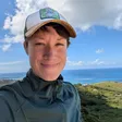 Michelle Weaver smiling in a trucker cap on a hilltop in St. Croix, with the sea behind