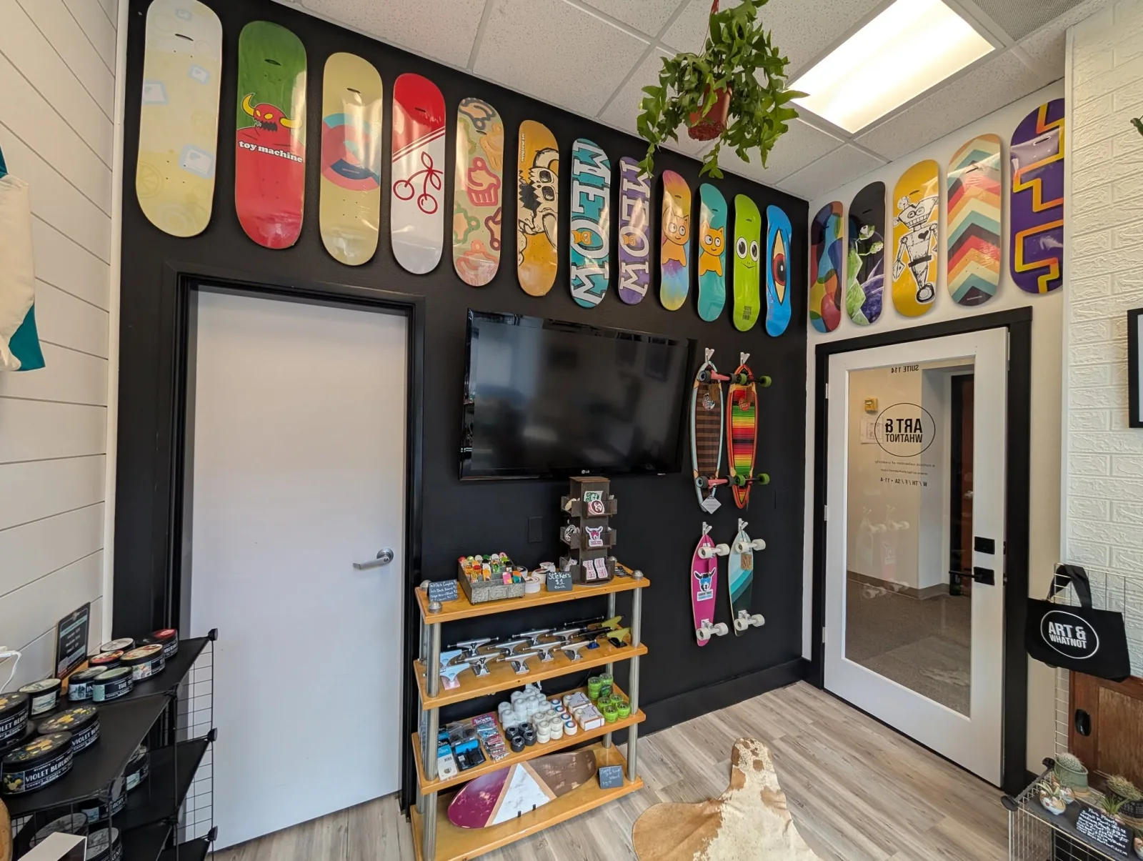 Inside the Art & WhatNot shop in Arlington: a wall of skateboard decks above the door, Weavie Board Co. decks on display, a shelf of skate hardware, and the front door with the shop logo